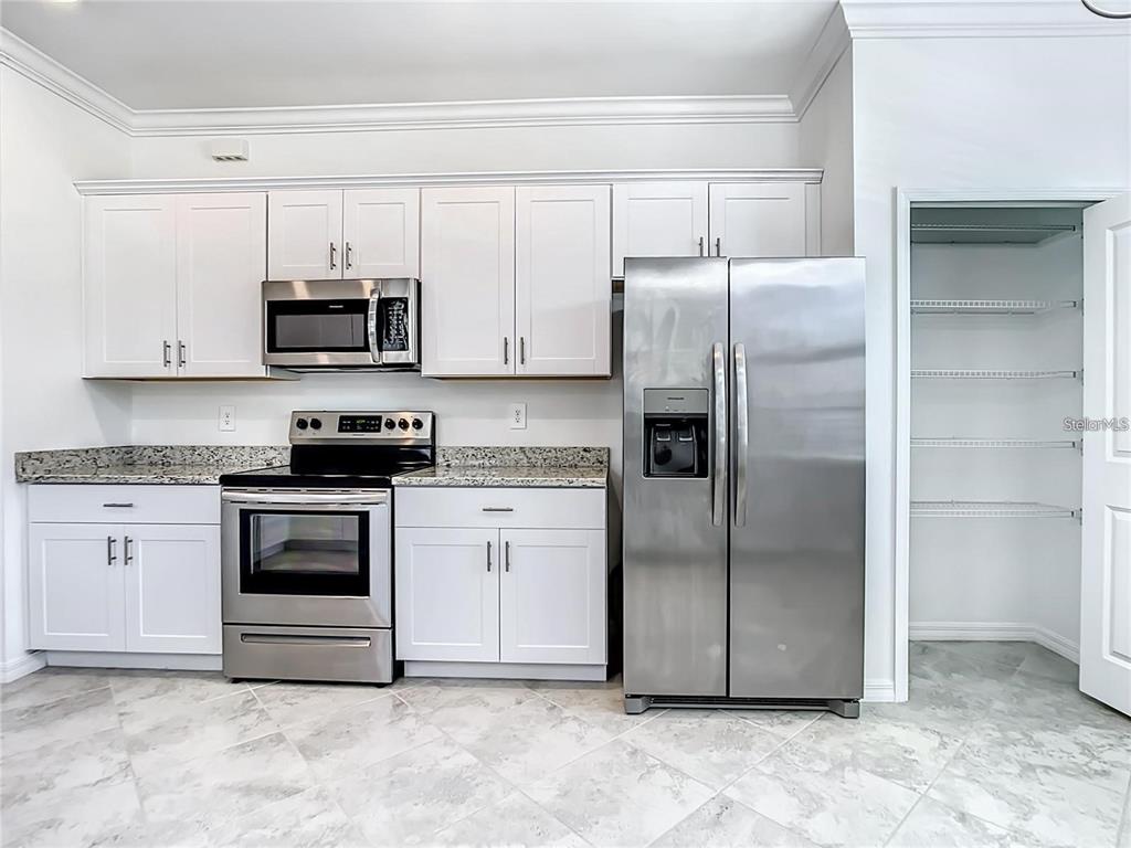 A kitchen features white cabinets, stainless steel appliances, granite countertops, and a walk-in pantry — 11100 BALFOUR STREET, VENICE, FL