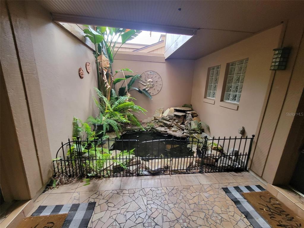An enclosed courtyard features a stone-lined koi pond, lush plants, and a metal safety fence — 101 CEDAR POINT LANE, LONGWOOD, FL