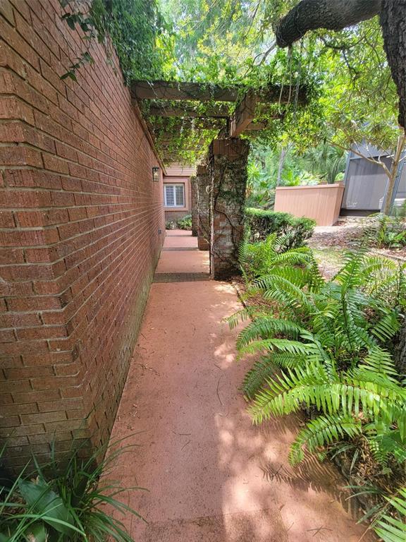 A brick walkway leads along the side of a house under a vine-covered wooden pergola — 101 CEDAR POINT LANE, LONGWOOD, FL
