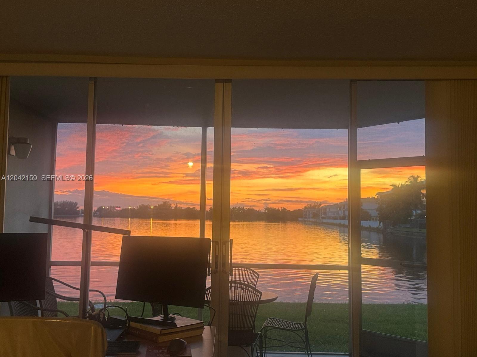 A view of a sunset over a lake seen through a sliding glass door — 1300 NE 191st St # A106, Miami FL 33179, MIAMI, FL