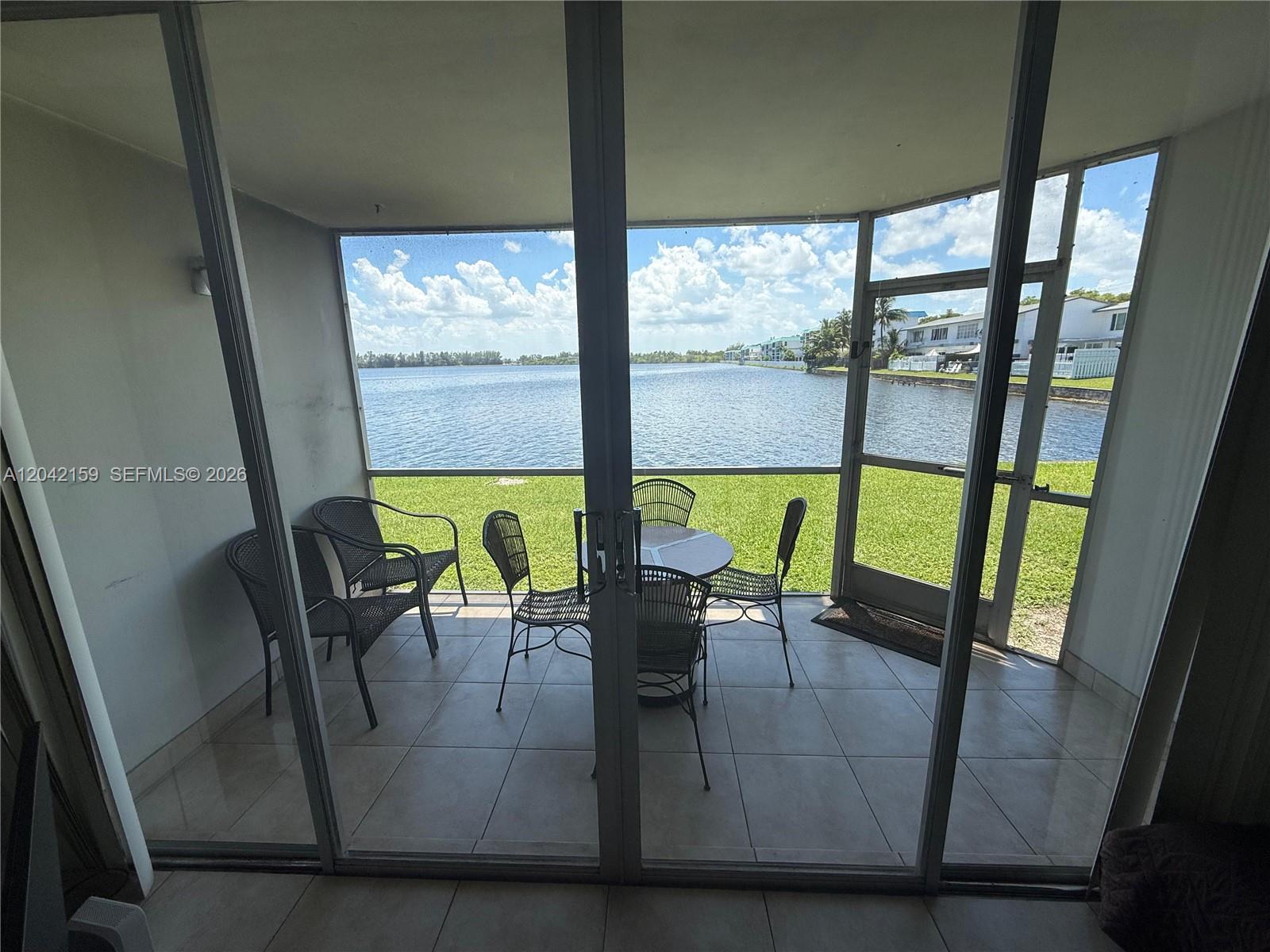 A screened-in patio features tile flooring, outdoor furniture, and a view of a lake — 1300 NE 191st St # A106, Miami FL 33179, MIAMI, FL