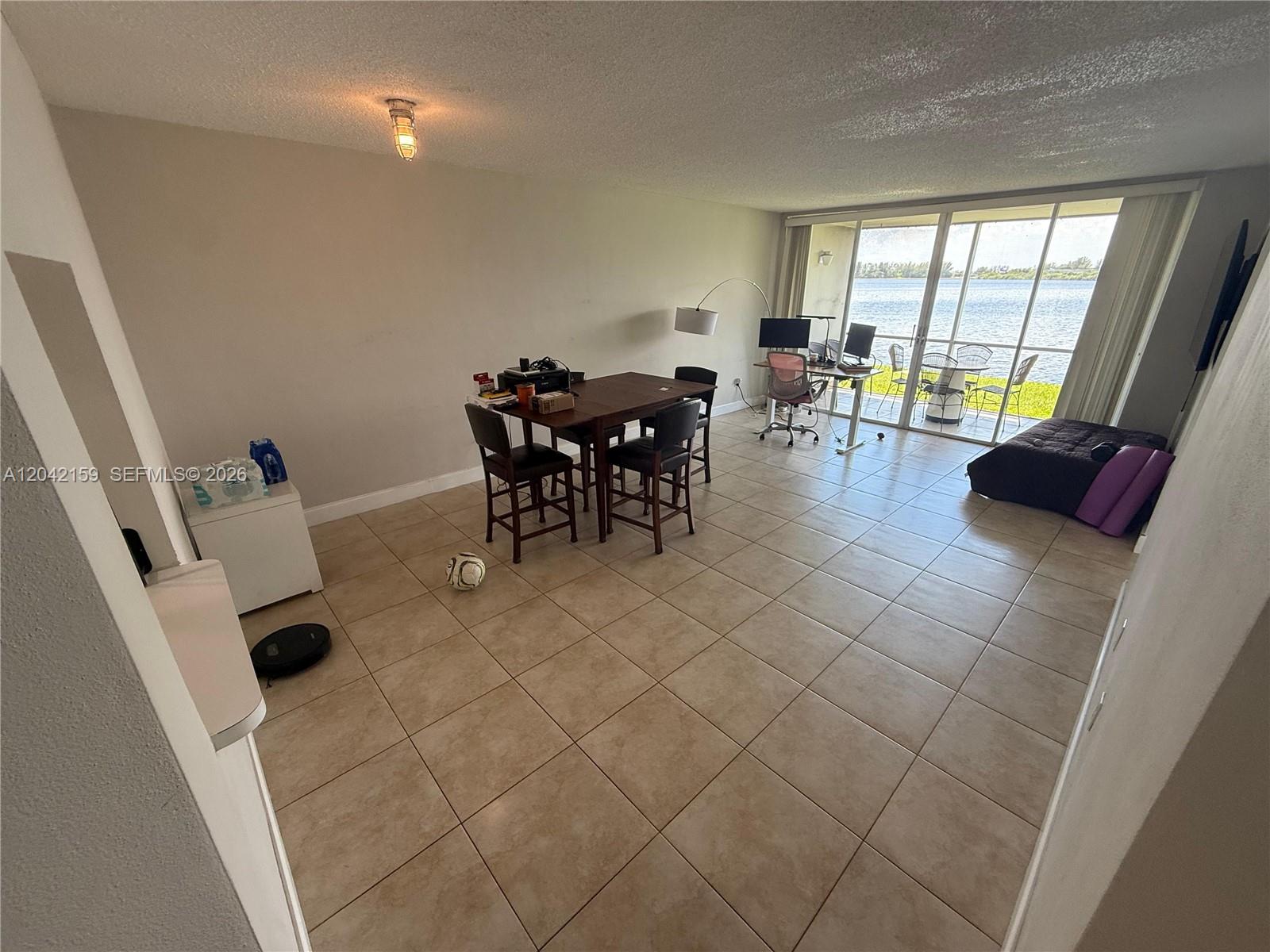 An open-concept living area features tile flooring, a dining set, and a waterfront balcony view — 1300 NE 191st St # A106, Miami FL 33179, MIAMI, FL