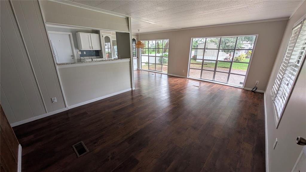 A living room with dark wood-look flooring, large windows, and an open view into the kitchen — 11716 E U.S. HIGHWAY 92, SEFFNER, FL
