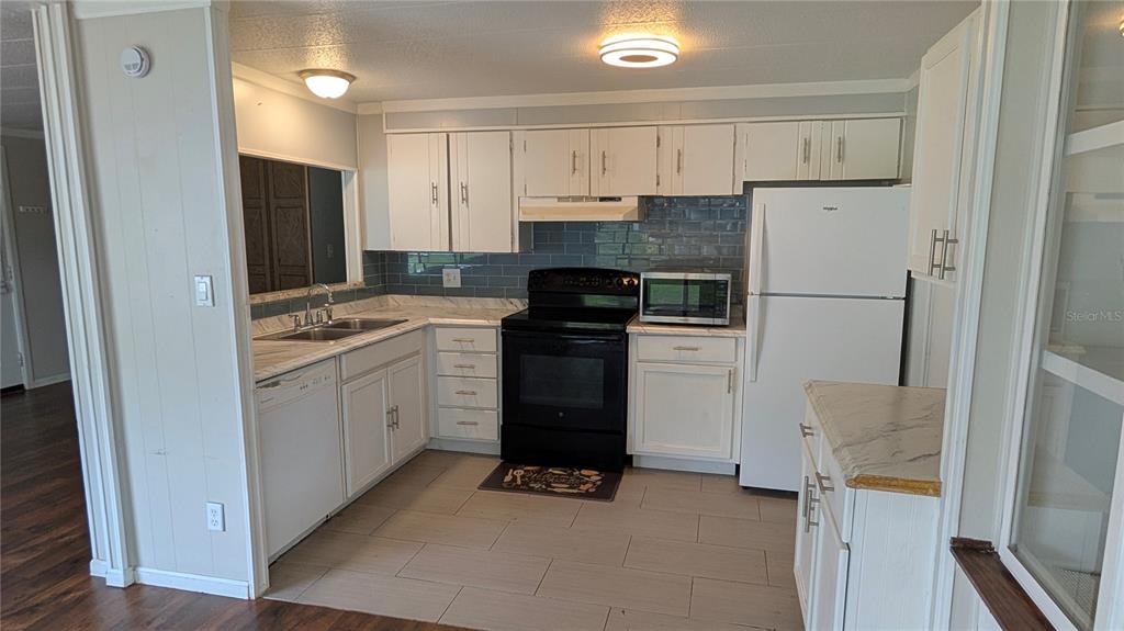 A kitchen features white cabinets, a black stove, a white refrigerator, and a blue backsplash — 11716 E U.S. HIGHWAY 92, SEFFNER, FL