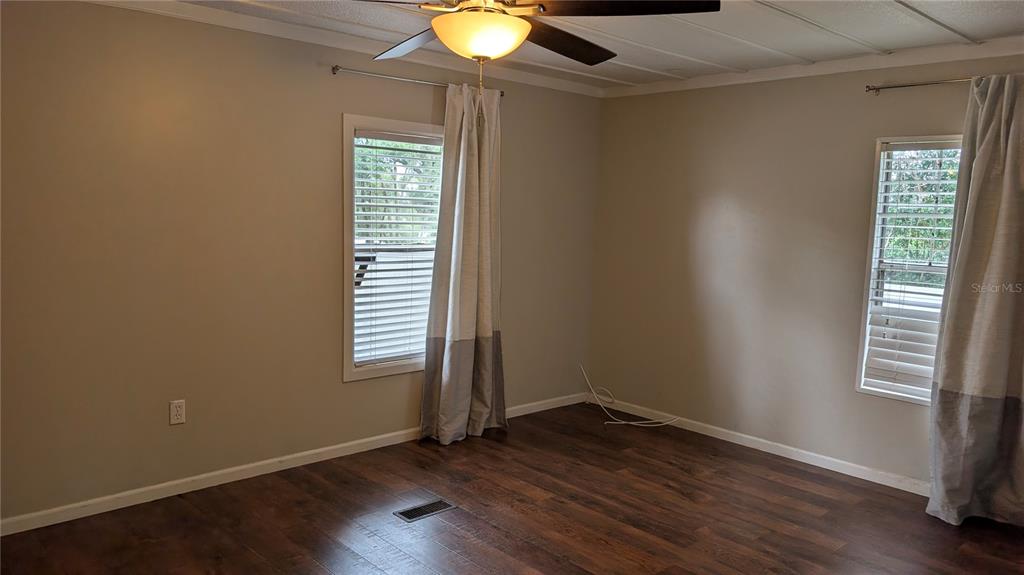 An empty bedroom features wood-look flooring, two windows with blinds and curtains, and a ceiling fan — 11716 E U.S. HIGHWAY 92, SEFFNER, FL