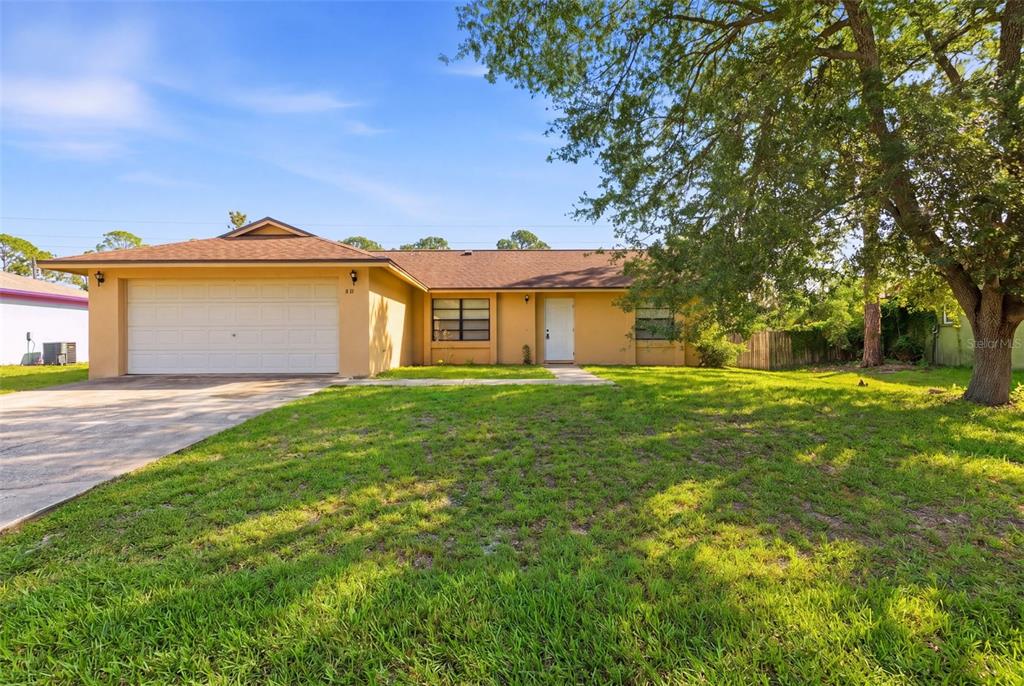 A single-story house with a tan exterior, a two-car garage, and a large front lawn — 871 LAMPLIGHTER DRIVE NW, PALM BAY, FL