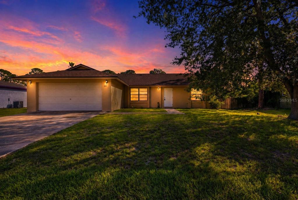 A single-story house with a garage and a large tree at sunset — 871 LAMPLIGHTER DRIVE NW, PALM BAY, FL