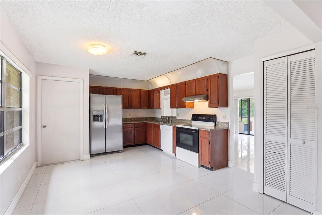 A kitchen with wood cabinets, stainless steel appliances, granite countertops, and white tile flooring — 871 LAMPLIGHTER DRIVE NW, PALM BAY, FL