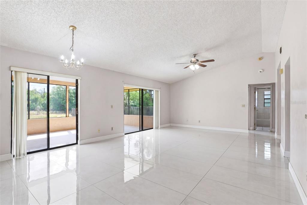 A spacious living room features white tile floors, a vaulted ceiling, and two sliding glass doors — 871 LAMPLIGHTER DRIVE NW, PALM BAY, FL