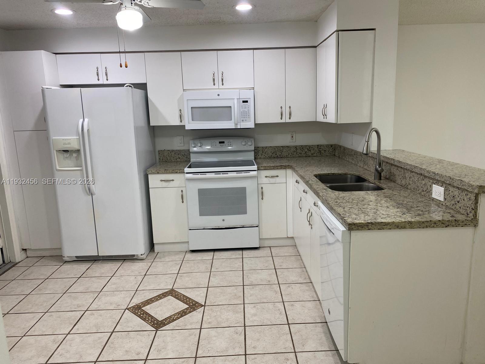 A kitchen features white cabinets, white appliances, granite countertops, and light-colored tiled flooring — 1384 Veracruz Ln # 7, Weston FL 33327, WESTON, FL
