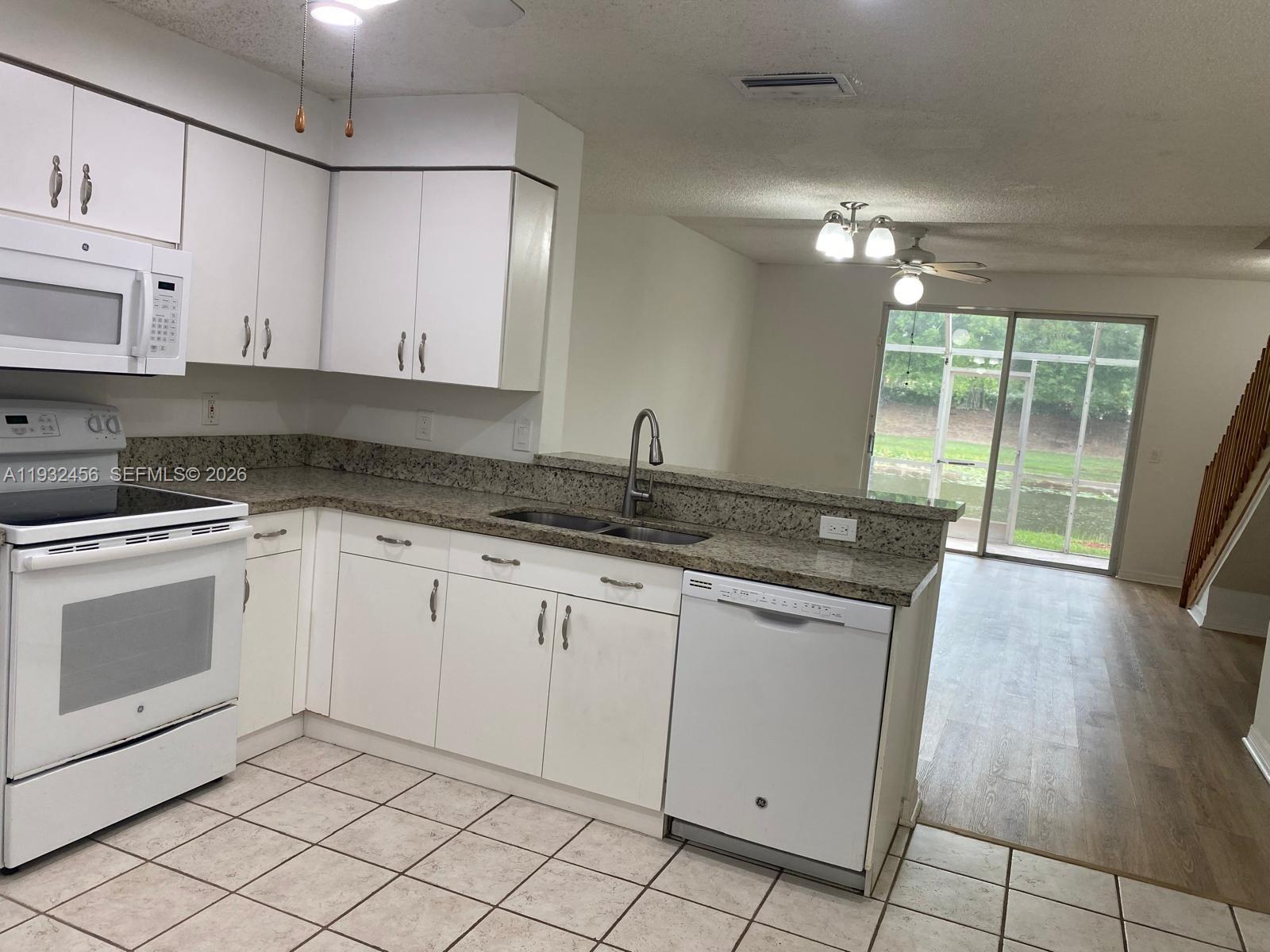 A kitchen with white cabinets, granite countertops, and a dishwasher overlooks a living area — 1384 Veracruz Ln # 7, Weston FL 33327, WESTON, FL