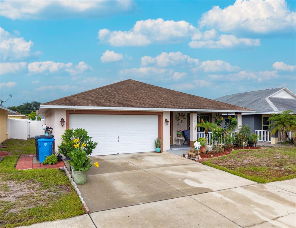 The exterior of a house features a garage, a covered porch, and several potted plants — 1128 SHARED PASSION ST, RUSKIN, FL
