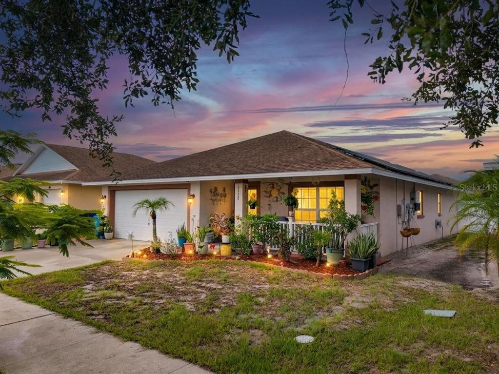 A covered front porch features a brown door, a sun wall decoration, and potted plants — 1128 SHARED PASSION ST, RUSKIN, FL