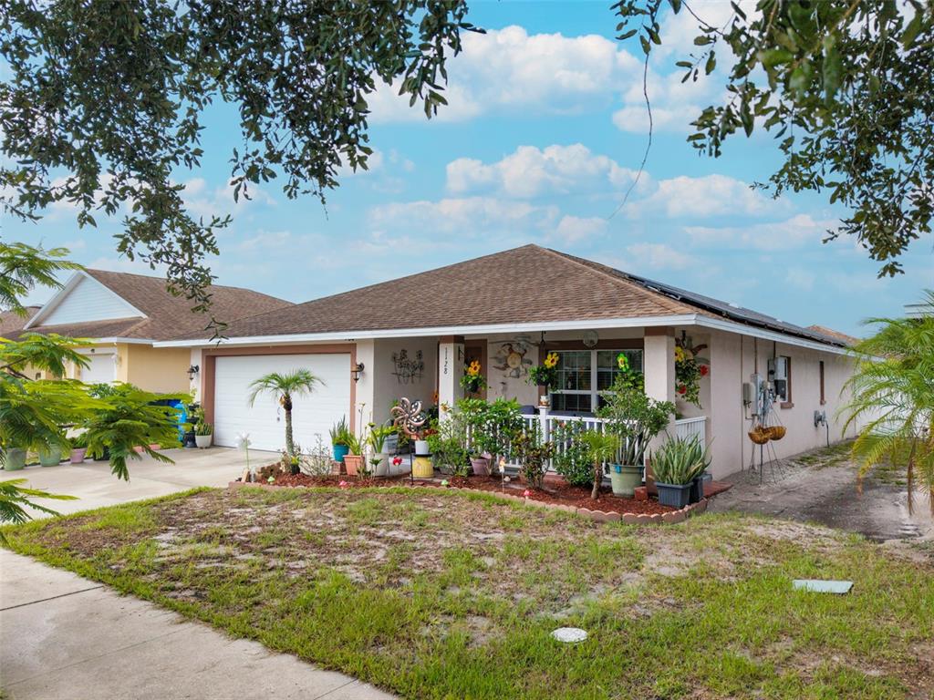 A covered porch features a brown front door, wicker furniture, and a ceiling fan — 1128 SHARED PASSION ST, RUSKIN, FL