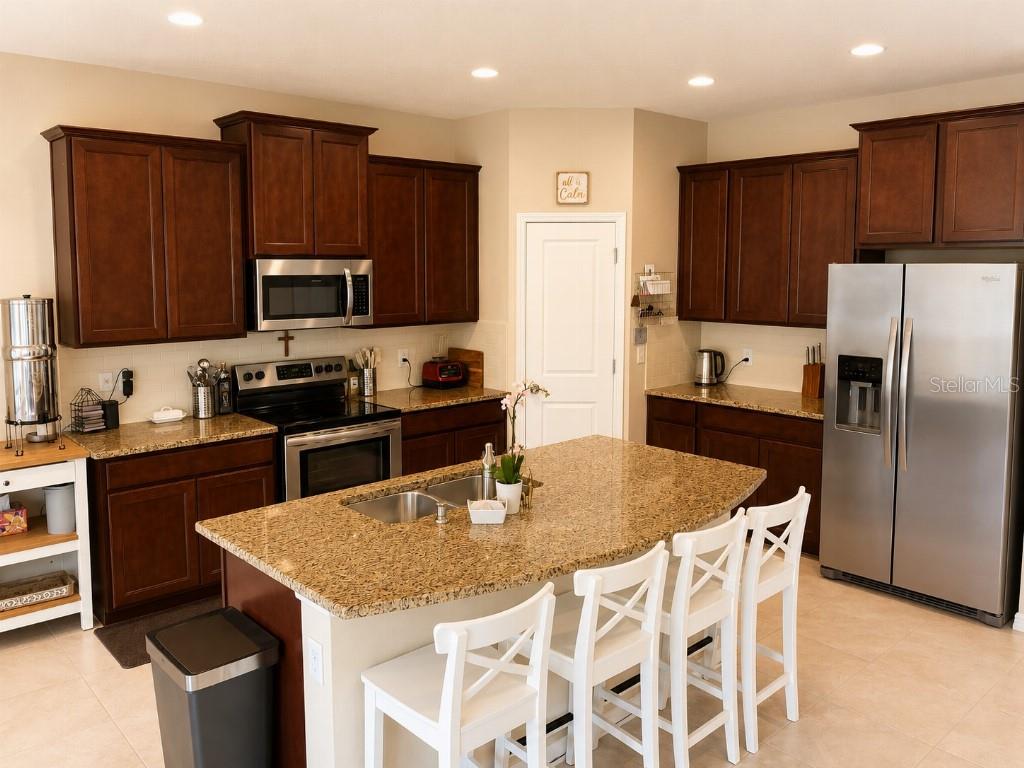 A kitchen features dark wood cabinets, granite countertops, a central island, and stainless steel appliances — 2296 MIDNIGHT PEARL DRIVE, SARASOTA, FL