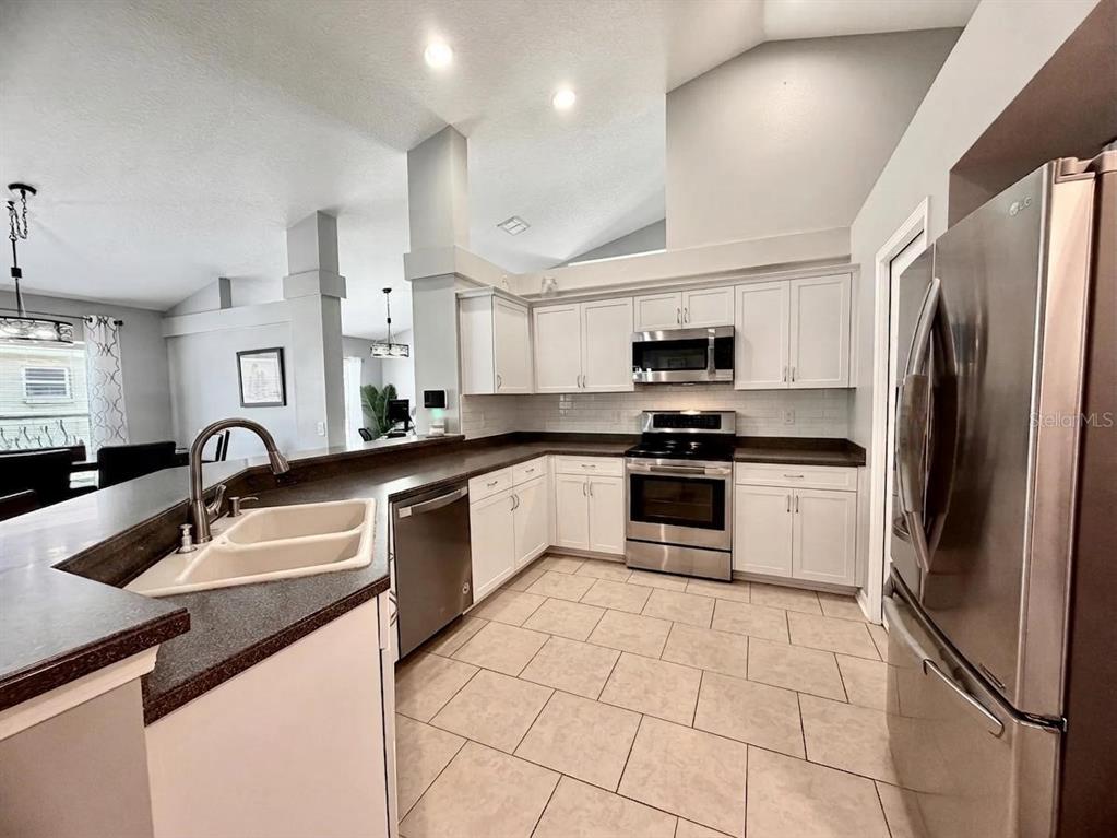 A kitchen features white cabinets, stainless steel appliances, dark countertops, and light tile flooring — 13449 MEADOW GOLF AVENUE, HUDSON, FL