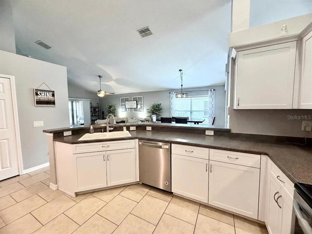 A kitchen with white cabinets, dark countertops, and stainless steel appliances overlooks a living area — 13449 MEADOW GOLF AVENUE, HUDSON, FL