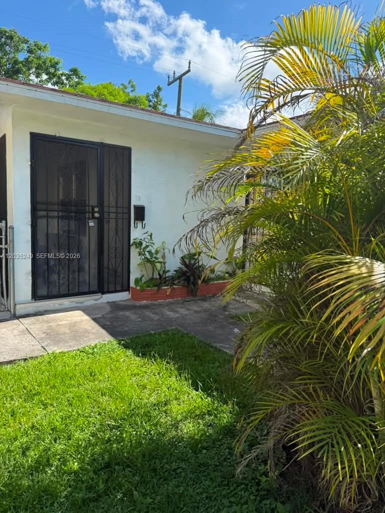 A white exterior wall features a black security door and a small garden bed — 78 NE 43rd St # 0, Miami FL 33137, MIAMI, FL