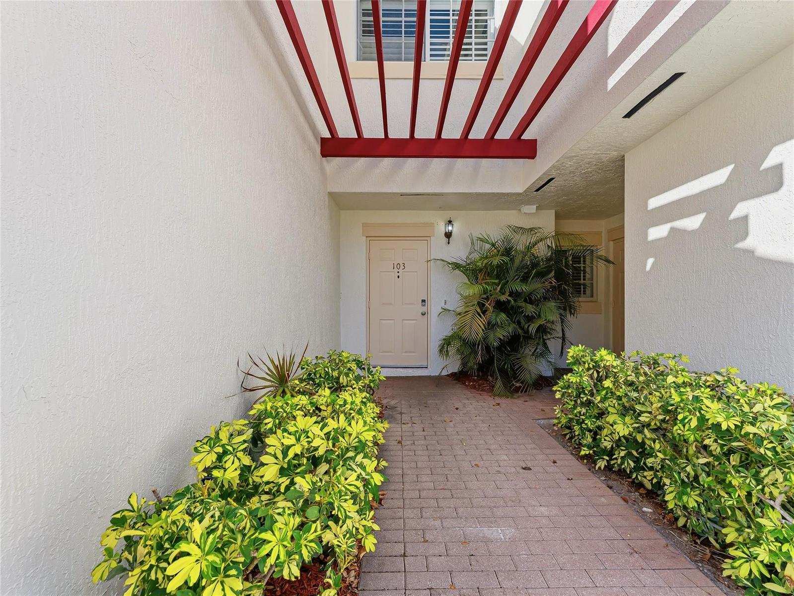A paved walkway leads to the front door of a residence with red overhead beams — 504 7th Square # 103, Vero Beach FL 32962, VERO BEACH, FL