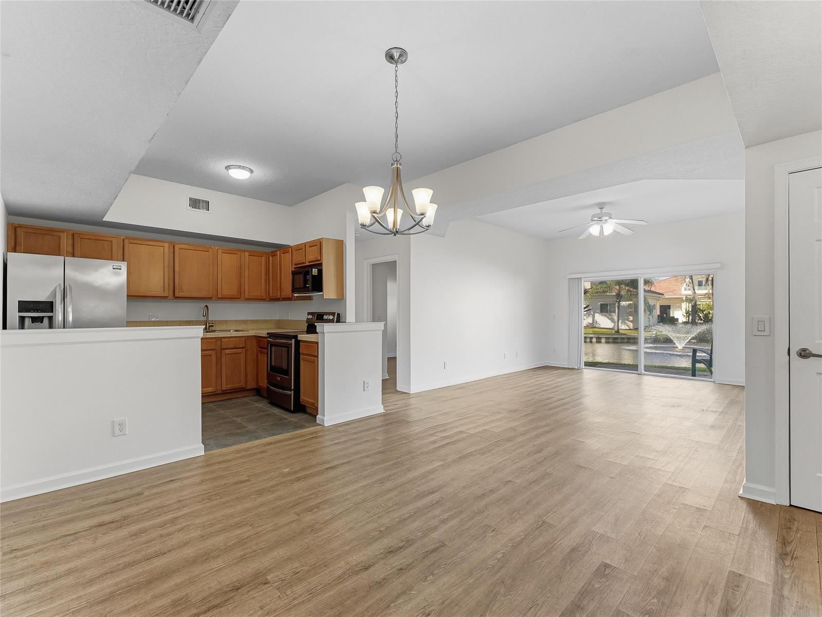 An open-concept kitchen with wood cabinets and stainless appliances overlooks a living area with flooring — 504 7th Square # 103, Vero Beach FL 32962, VERO BEACH, FL