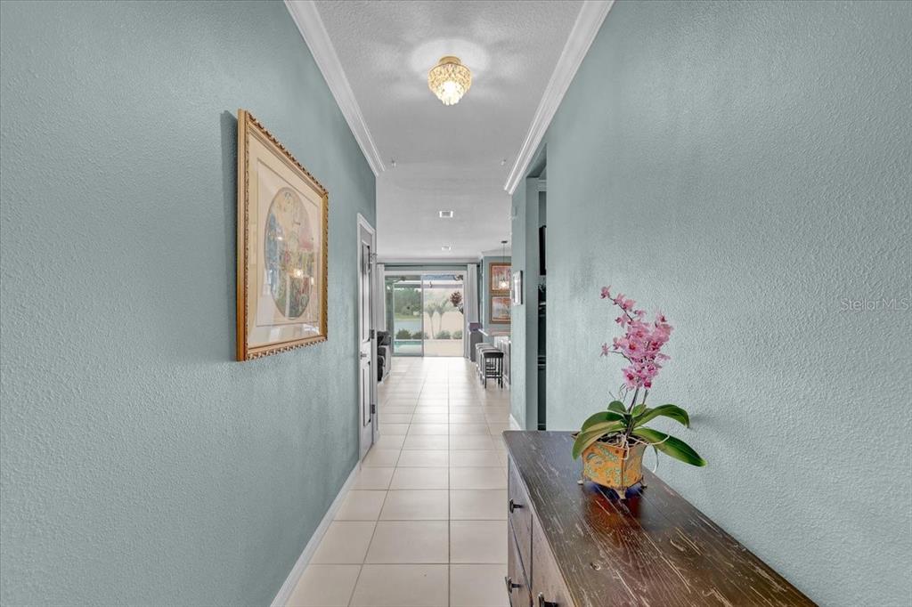 A hallway with light blue walls, tile flooring, and a wooden console table with orchids — 3921 MOSSY LIMB COURT, PALMETTO, FL