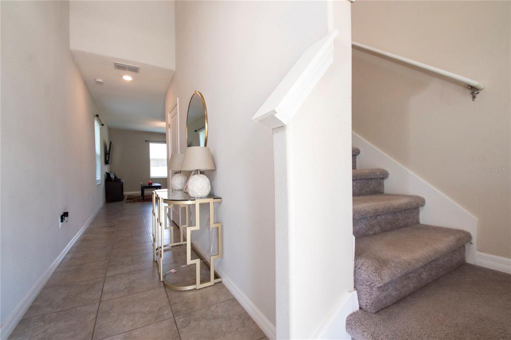 A tiled entryway features a console table with lamps and a carpeted staircase — 10202 COOL WATERLILY AVENUE, RIVERVIEW, FL