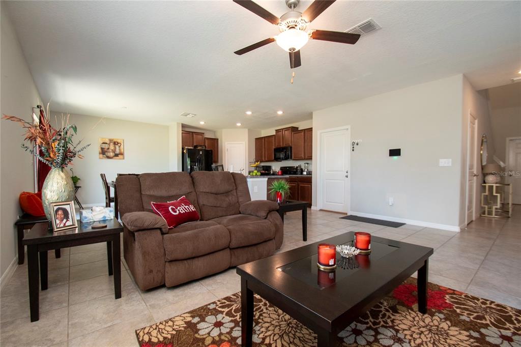 A living room with tile floors, a brown loveseat, and an open kitchen in the background — 10202 COOL WATERLILY AVENUE, RIVERVIEW, FL