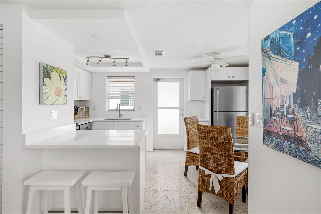A bright kitchen features white cabinets, a breakfast bar, and a dining area with wicker chairs — 6154 MIDNIGHT PASS ROAD UNIT A-3, SARASOTA, FL