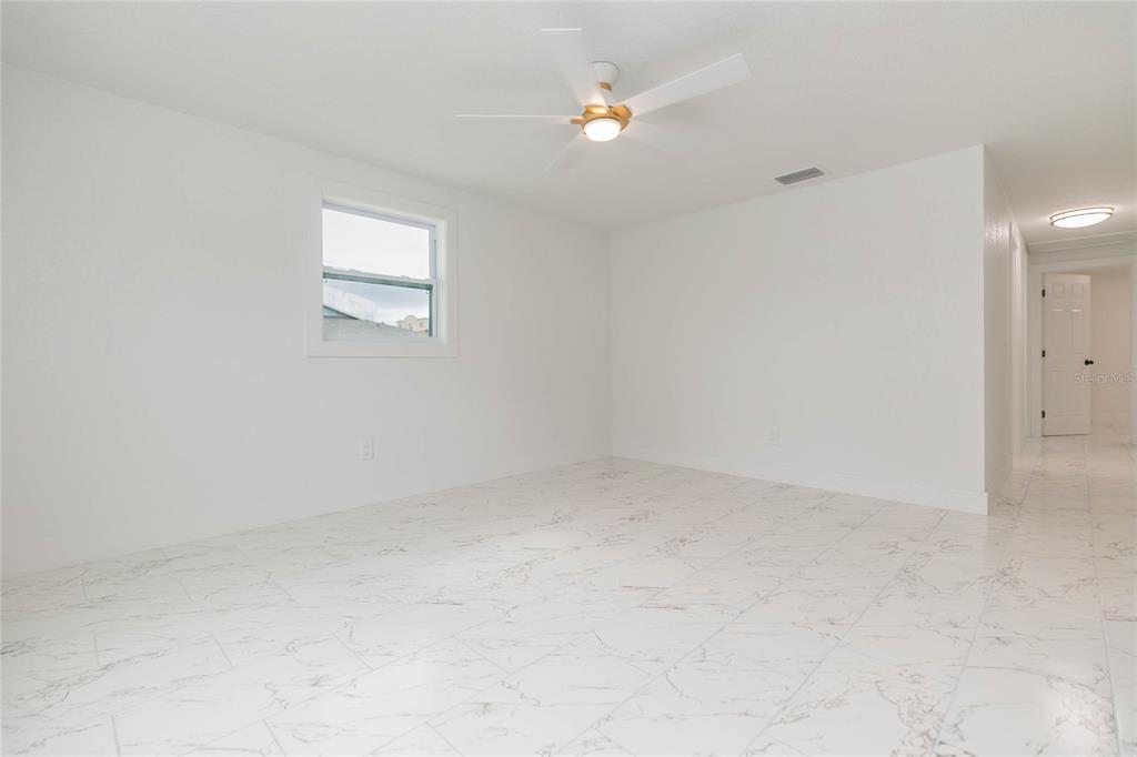 A bright, empty room features white walls, a ceiling fan, and white marble-patterned tile flooring — 8723 N RIVER FOREST CIRCLE, TAMPA, FL