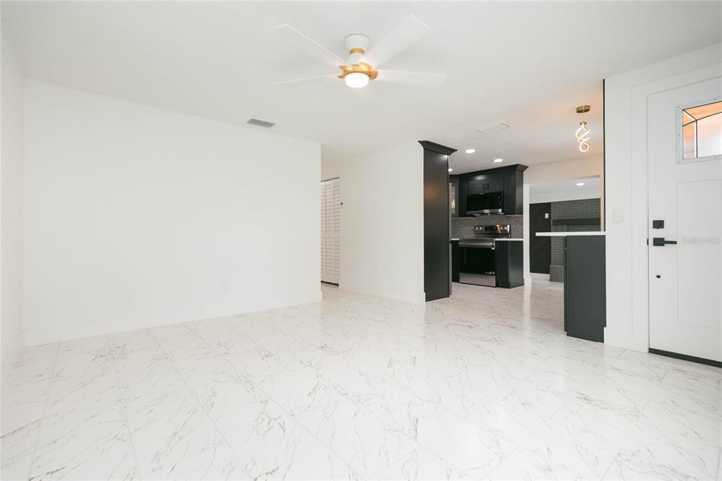 A bright room with white marble-look tile flooring, a ceiling fan, and a modern kitchen — 8723 N RIVER FOREST CIRCLE, TAMPA, FL