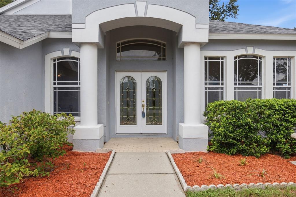 A gray house exterior features a covered entryway with white columns and double glass doors — 4634 RIVER OVERLOOK DRIVE, VALRICO, FL