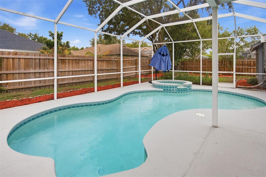 A screened-in backyard features a swimming pool with an attached hot tub and wood fencing — 4634 RIVER OVERLOOK DRIVE, VALRICO, FL