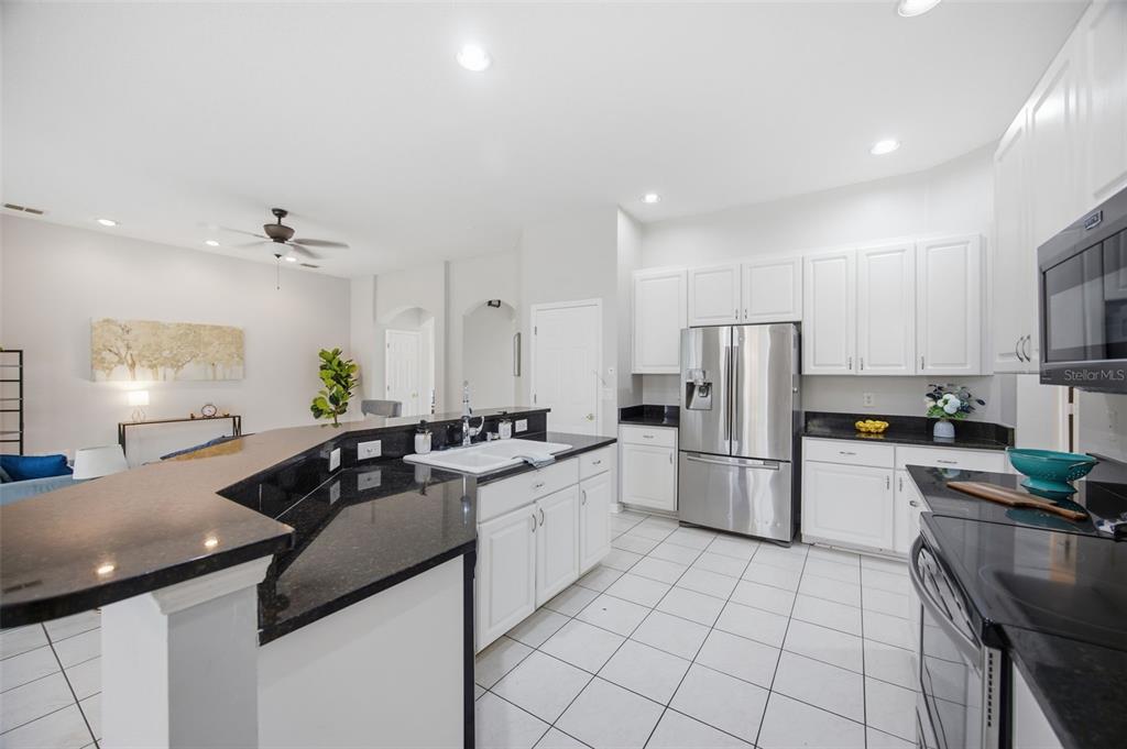 A kitchen with white cabinets, black granite countertops, stainless steel appliances, and white tile flooring — 4634 RIVER OVERLOOK DRIVE, VALRICO, FL