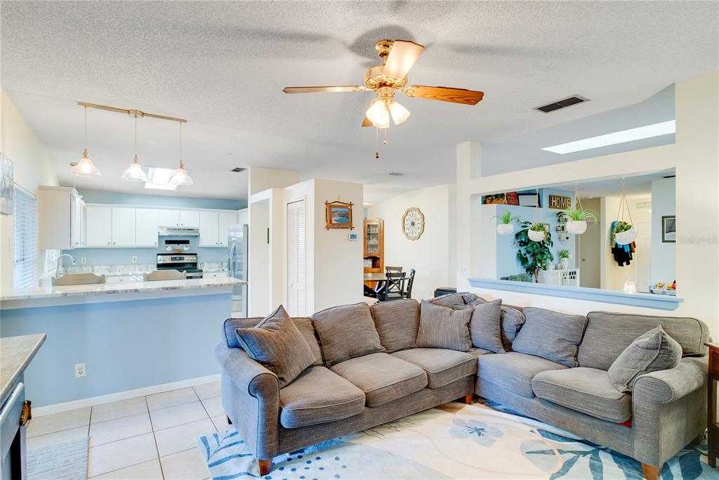 A living room with a gray sectional sofa opens to a kitchen with white cabinets — 1801 CONCORD DRIVE, APOPKA, FL