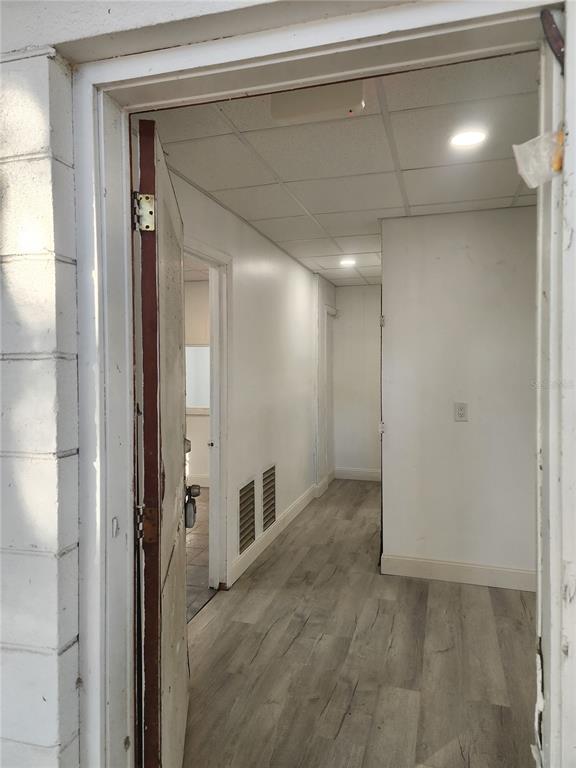 A view through an open doorway into a hallway with light wood-look flooring and ceiling tiles — 1780 E DUVAL STREET UNIT 6, LAKE CITY, FL