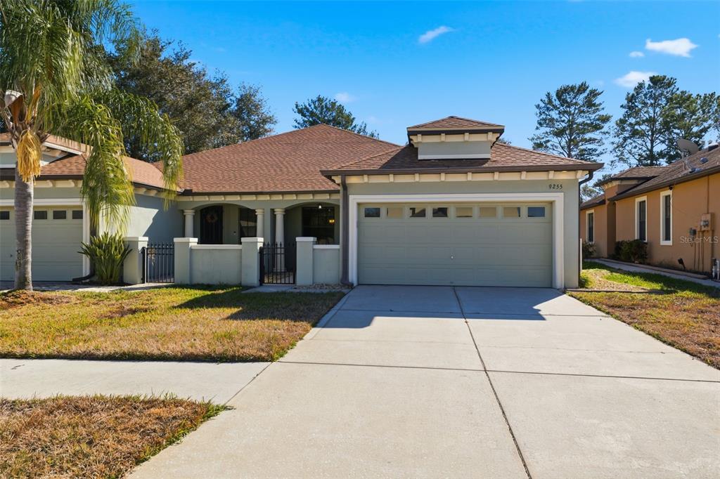 A single-story house with a two-car garage, a gated courtyard entrance, and a palm tree — 9255 SOUTHERN CHARM CIRCLE, BROOKSVILLE, FL