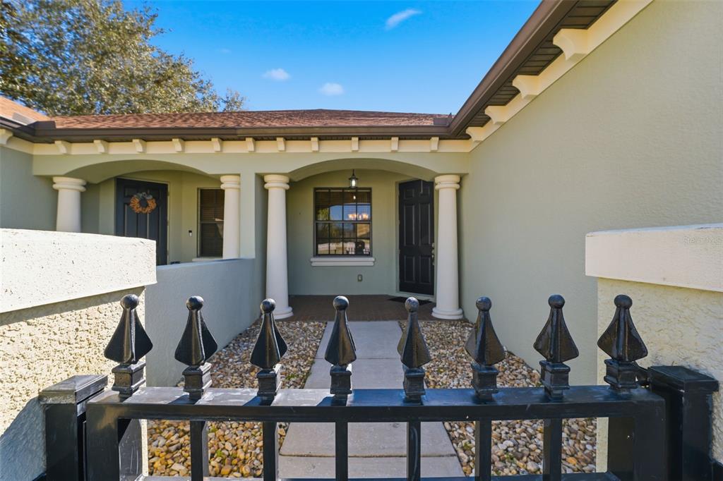 A gated courtyard leads to the front entrance of a house with light-colored stucco walls — 9255 SOUTHERN CHARM CIRCLE, BROOKSVILLE, FL
