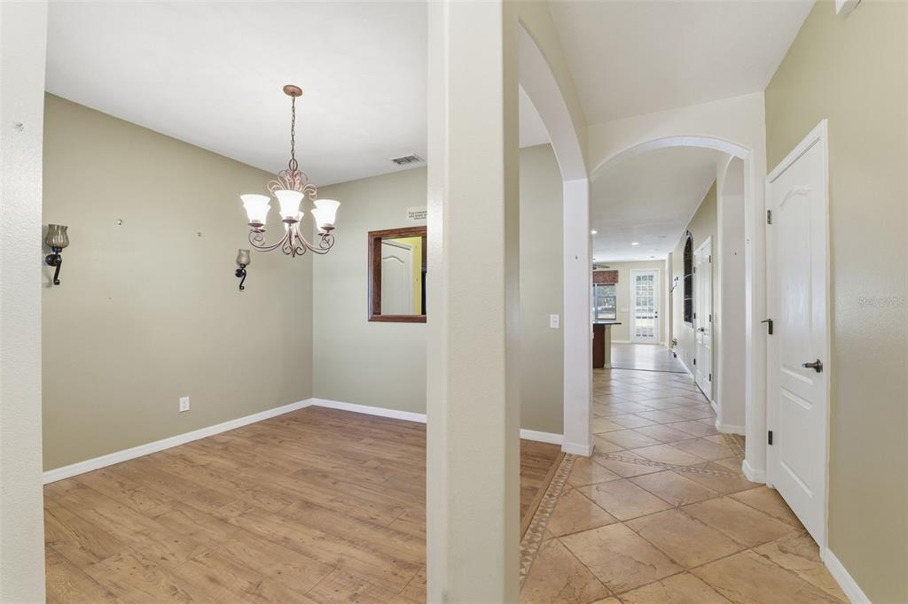 A dining room with wood-look flooring and a chandelier sits beside a tiled hallway — 9255 SOUTHERN CHARM CIRCLE, BROOKSVILLE, FL