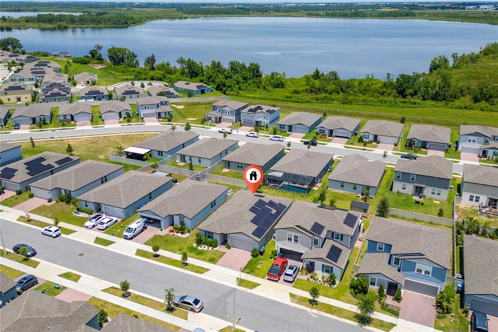 An aerial view shows a suburban neighborhood with houses featuring solar panels near a lake — 3053 CASSIDY LANE, HAINES CITY, FL