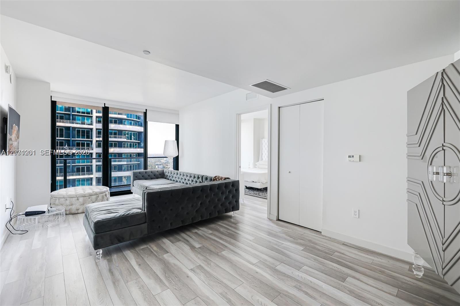 A modern living room features a grey tufted sectional, light wood flooring, and floor-to-ceiling windows — 1300 S Miami Ave # 3709, Miami FL 33130, MIAMI, FL