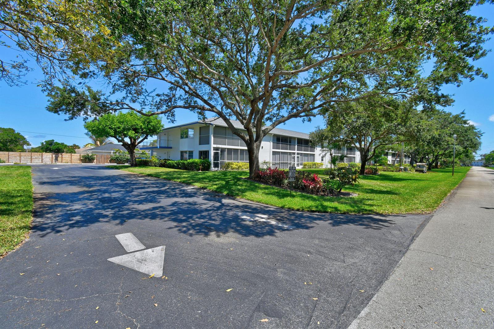 A multi-story apartment building with screened balconies sits behind a paved road with directional arrows — 9 Garden Street # 204j, Tequesta FL 33469, TEQUESTA, FL