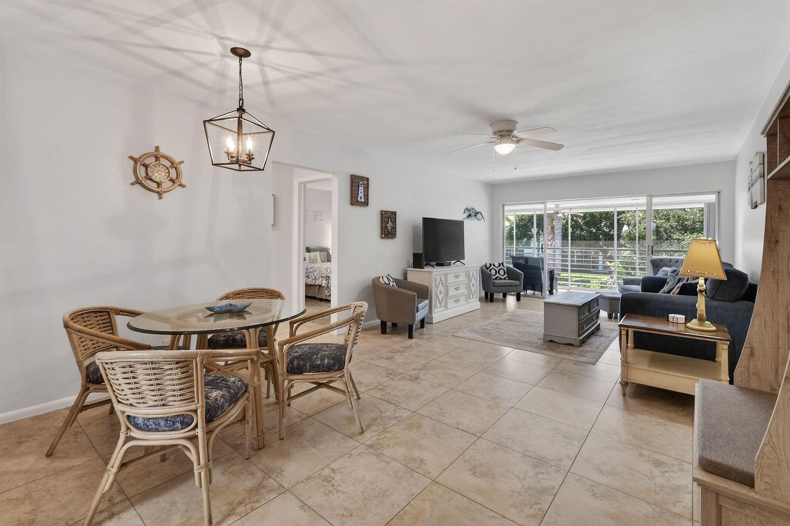 A living and dining area with tile floors, wicker chairs, and a sliding glass door — 9 Garden Street # 204j, Tequesta FL 33469, TEQUESTA, FL