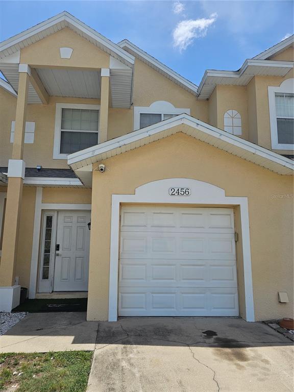 The exterior of a two-story beige townhouse features a single-car garage and a front door — 2456 TEMPLE GROVE LANE, KISSIMMEE, FL