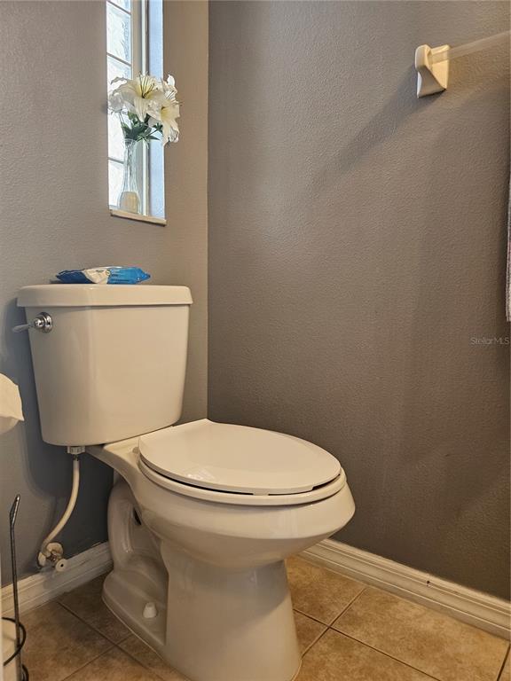A bathroom features a white toilet, gray walls, tile flooring, and a window with flowers — 2456 TEMPLE GROVE LANE, KISSIMMEE, FL