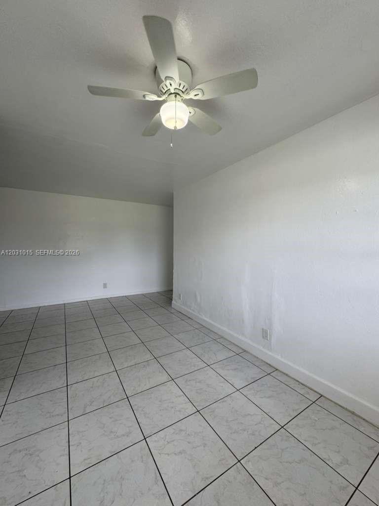 An empty room features white walls, a ceiling fan, and light-colored tiled flooring — FORT LAUDERDALE, FL