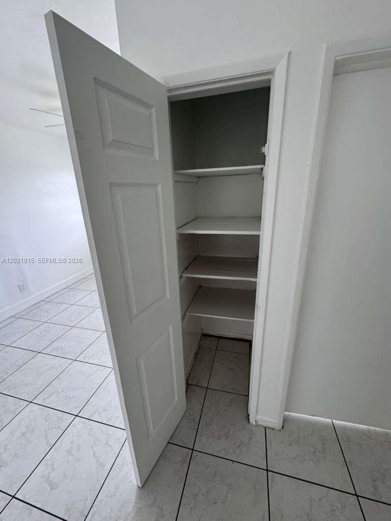 An open closet with multiple white shelves stands in a room with tiled flooring — FORT LAUDERDALE, FL