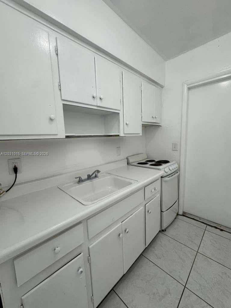 A small kitchen features white cabinets, a white sink, and a white electric stove — FORT LAUDERDALE, FL