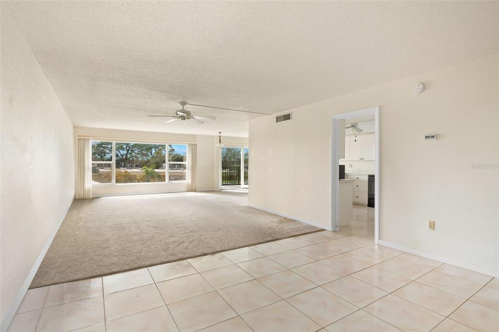 A living room with beige carpet and tile flooring features a large window and ceiling fan — 225 COUNTRY CLUB DRIVE UNIT F-1401, LARGO, FL