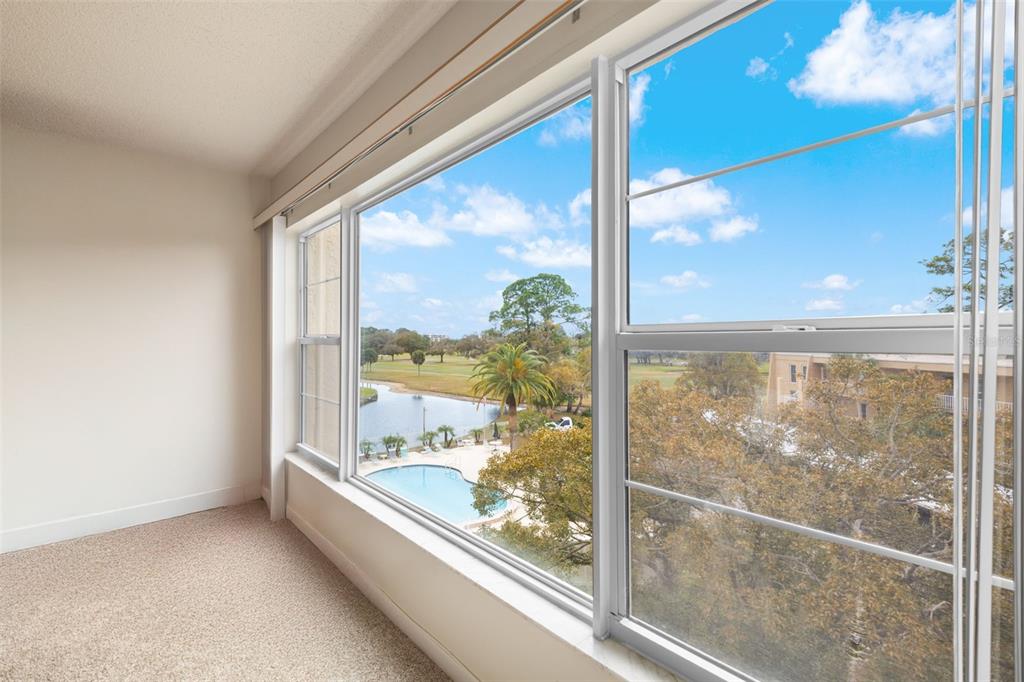 A carpeted room with large windows overlooking a swimming pool, a pond, and a golf course — 225 COUNTRY CLUB DRIVE UNIT F-1401, LARGO, FL