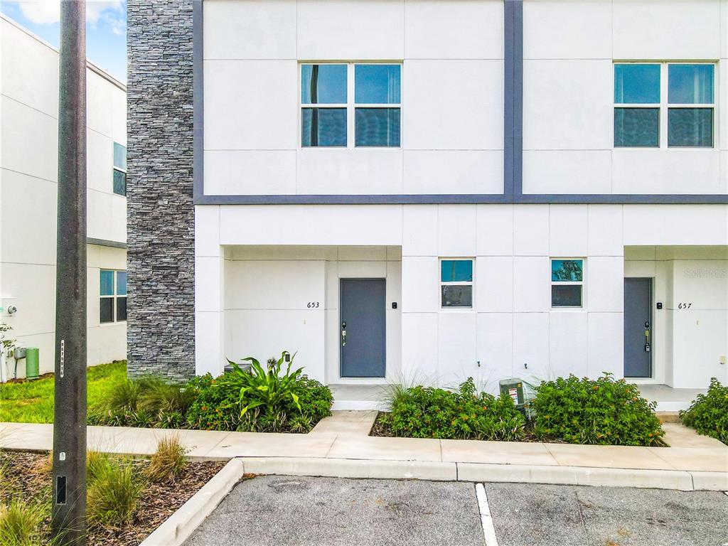 The exterior of a modern two-story townhouse with white panels and a stone accent wall — 653 TRIKOMO DRIVE, DAVENPORT, FL